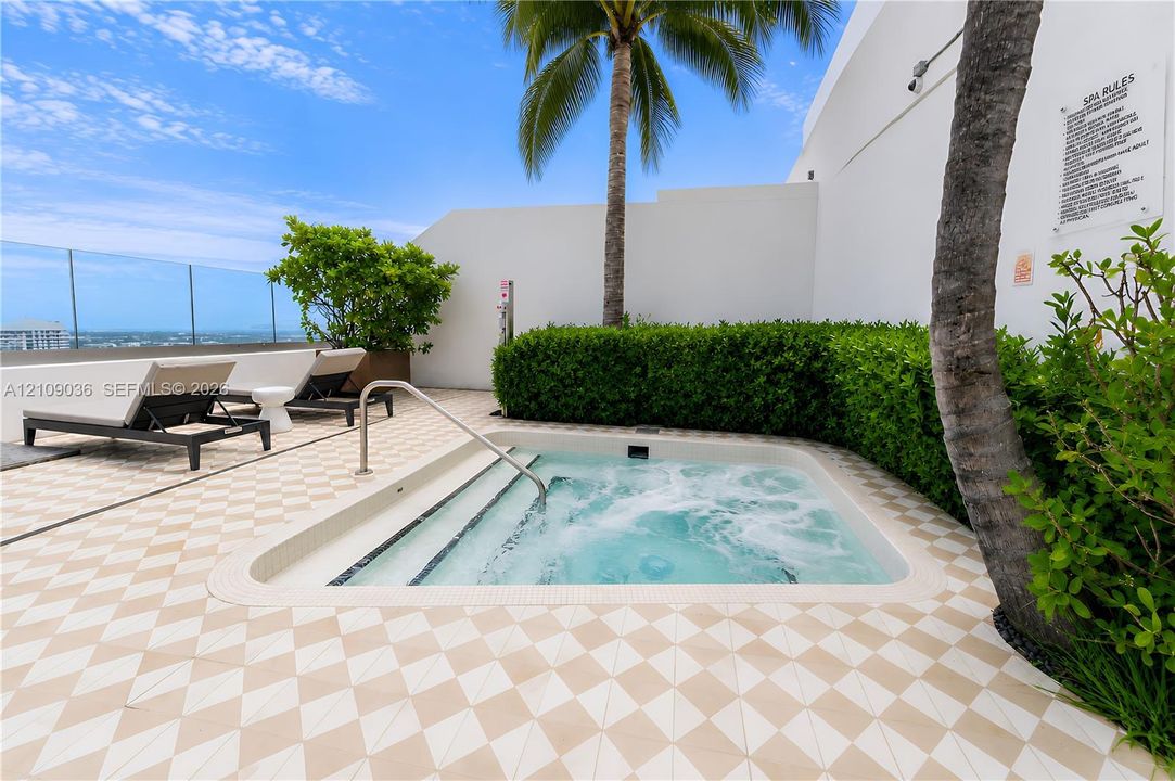 Rooftop terrace featuring an in-ground spa, patterned tile flooring, glass perimeter railing, and integrated landscaping