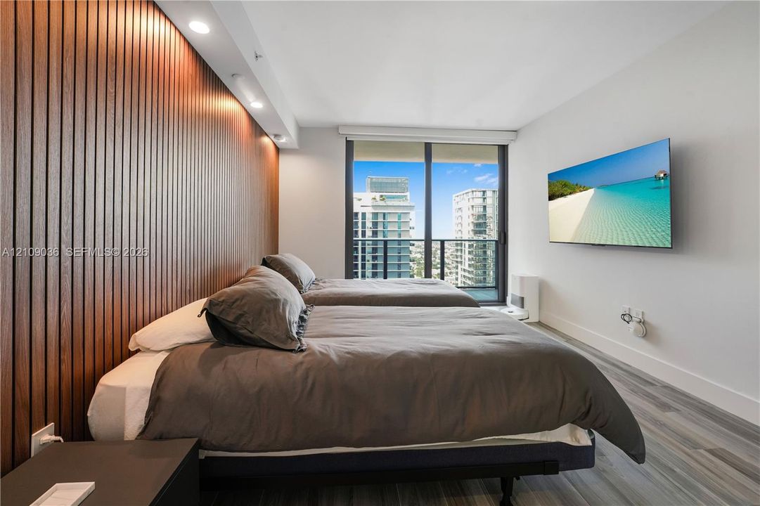 Floor-to-ceiling slatted wood-finish accent wall with integrated recessed lighting, wood-finish flooring, and large-format sliding glass door leading to a balcony