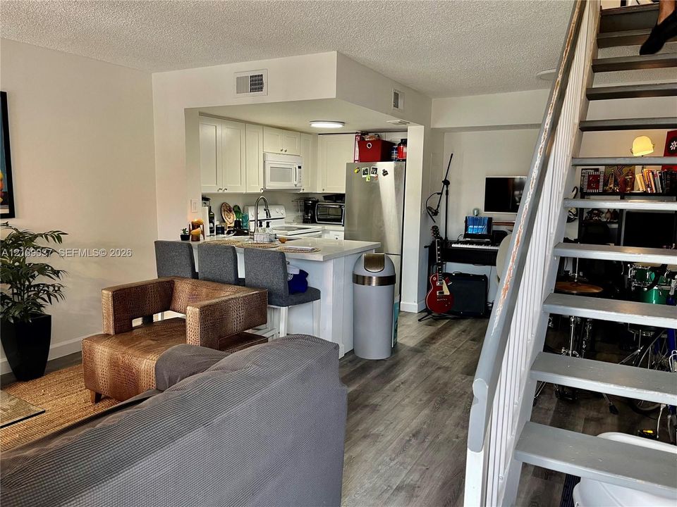Open-concept floor plan featuring wood-finish flooring, white kitchen cabinetry, a breakfast bar, and a staircase with painted wood steps and a white railing