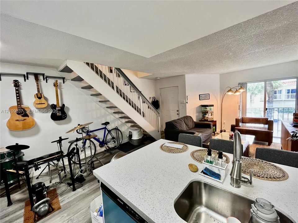 Open-concept kitchen featuring a solid surface countertop, undermount stainless steel sink with a high-arch gooseneck faucet, and wood-finish flooring