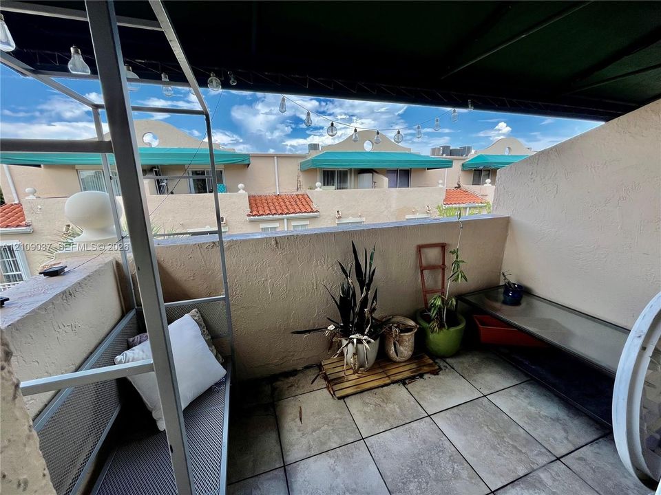 Covered balcony with square tile flooring, concrete partition walls, and overhead string lighting