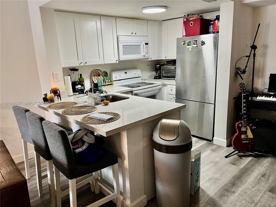 Kitchen featuring white shaker-style cabinetry, a stone-surface breakfast bar, a stainless steel refrigerator, and wood-finish flooring