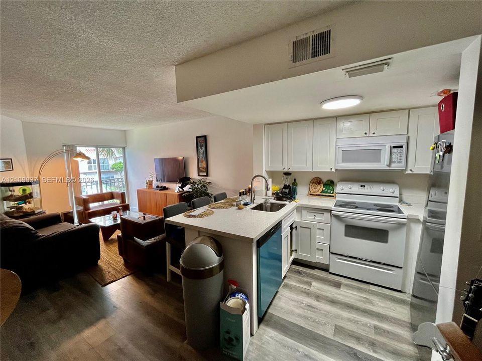 Kitchen featuring white cabinetry, solid-surface countertops, wood-finish flooring, and built-in appliances including an over-the-range microwave