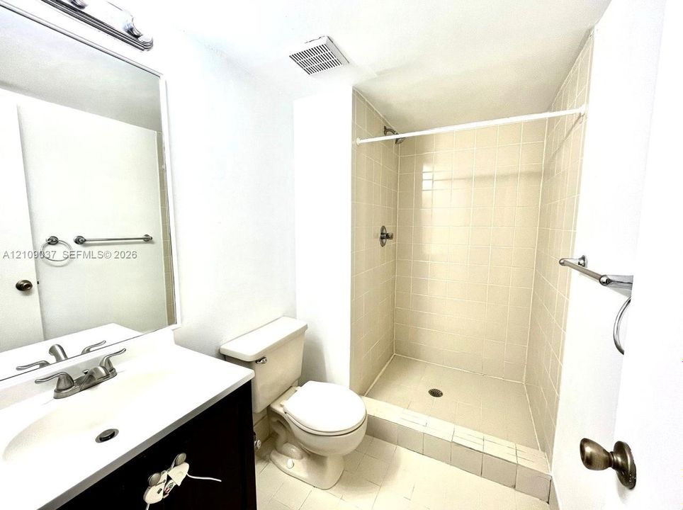 Bathroom featuring a dark-finish vanity with a white countertop, large wall-mounted mirror, ceramic-tiled shower enclosure, and tiled flooring