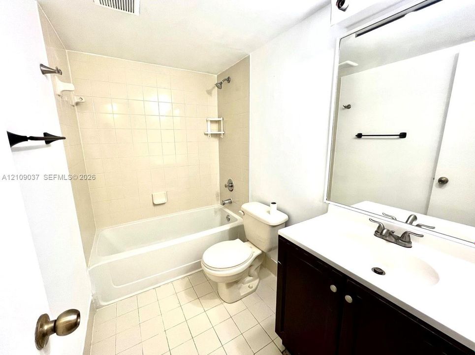 Bathroom featuring a dark-finish vanity with a solid-surface countertop, white tile flooring, and a combined tub and shower enclosure with tile surround