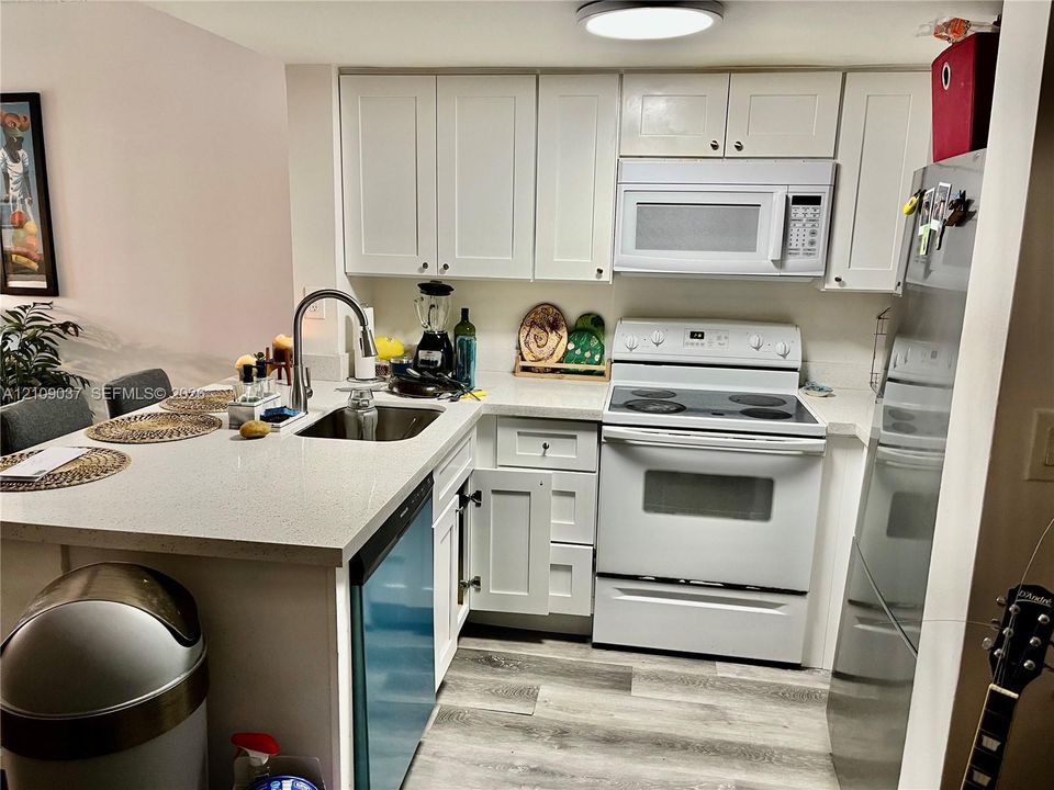 Kitchen featuring white cabinetry, solid-surface countertops, wood-finish flooring, stainless steel sink with high-arc faucet, and white appliances including a range and over-the-range microwave