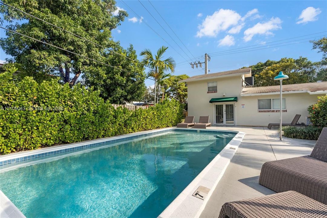 In-ground swimming pool with a concrete surround, enclosed by mature perimeter hedging and established palm trees