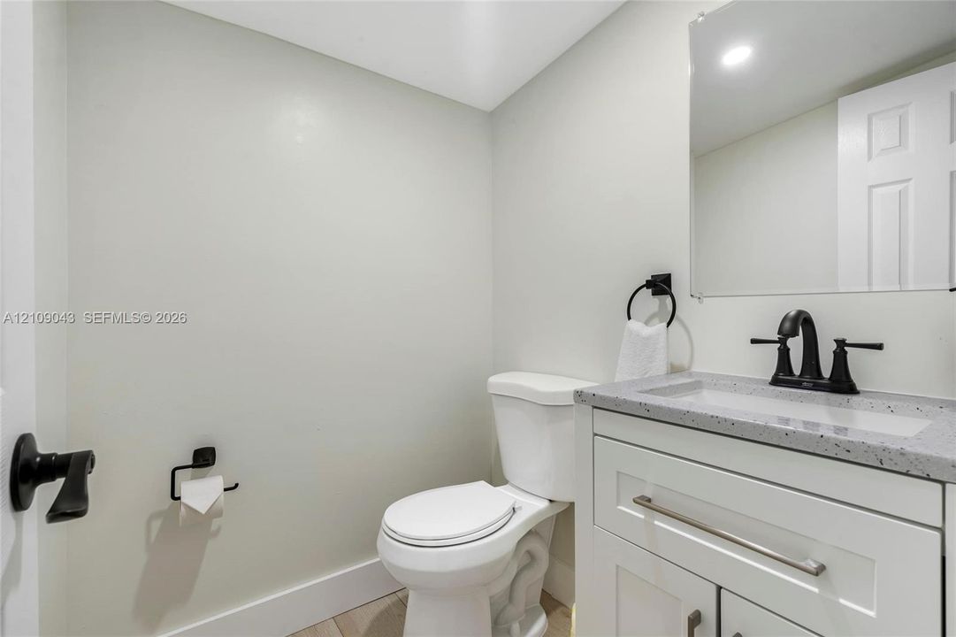 White vanity with speckled composite countertop, undermount sink, matte black faucet, wall-mounted mirror, and matching matte black hardware