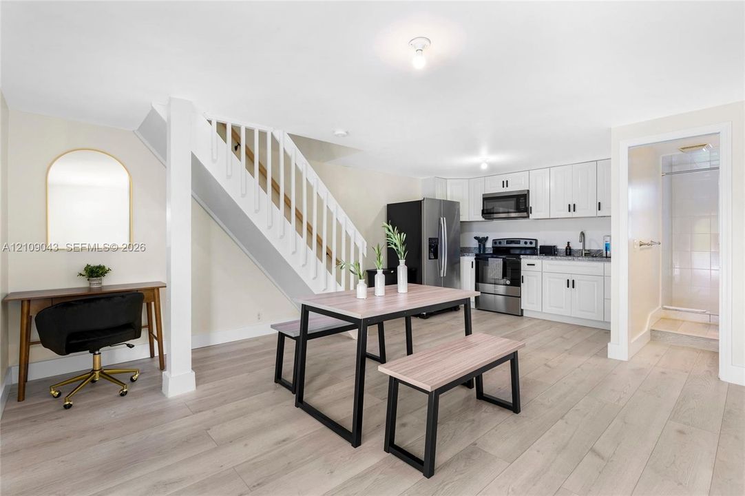 Open-concept kitchen featuring white shaker-style cabinetry, stainless steel appliances, and wood-finish flooring, complemented by a staircase with white balusters