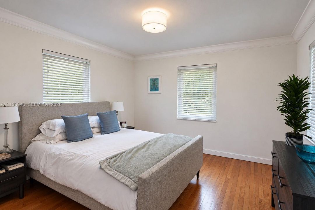 Neutral-toned room featuring hardwood flooring, crown molding, three windows with horizontal blinds, and a drum-style ceiling light fixture