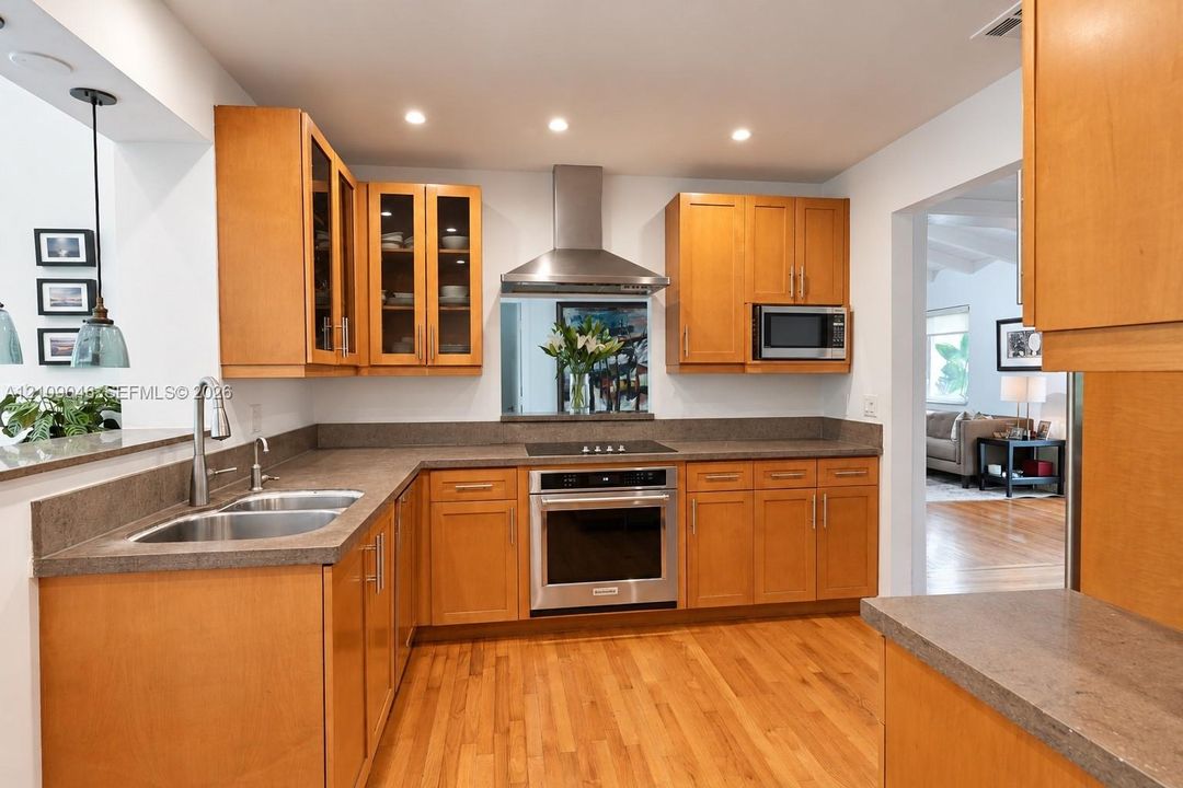 Kitchen featuring natural wood-finish cabinetry, solid surface countertops, stainless steel appliances, glass-front upper cabinets, and wood-finish flooring
