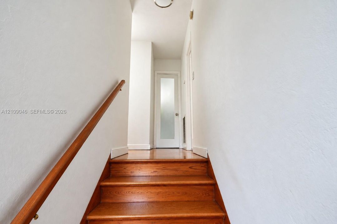 Staircase featuring wood-finish treads, a matching wood handrail, and a single-panel door with a frosted glass insert