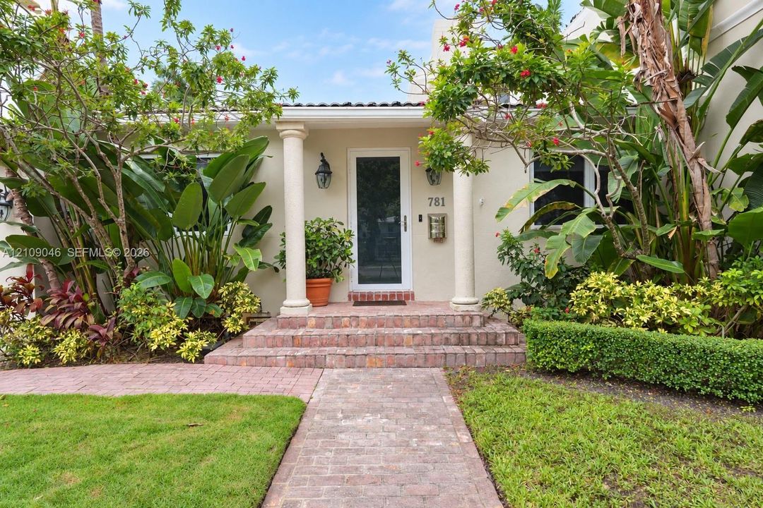 Covered entryway featuring classic columns, brick stairs, and a paved walkway, complemented by mature landscaping