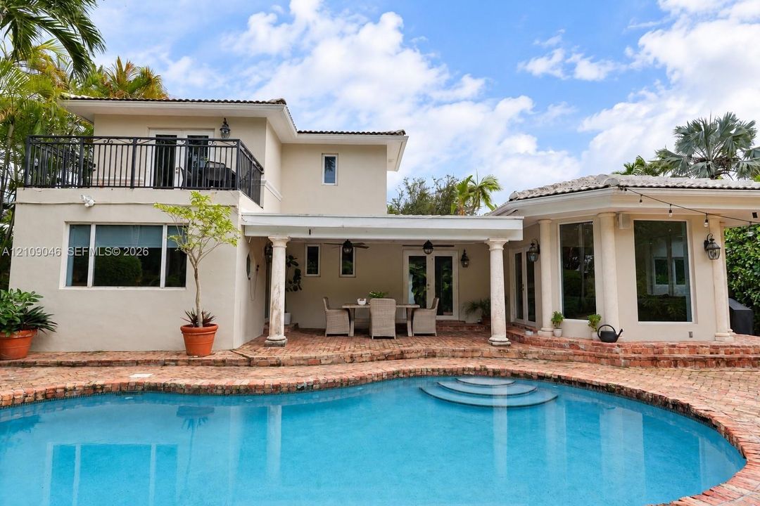 Exterior featuring a swimming pool with integrated steps, a brick-paved patio, a covered lanai supported by classical columns, and an upper-level balcony with metal railings