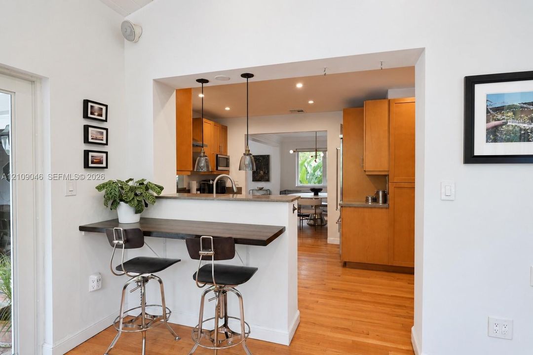 Kitchen featuring wood-finish cabinetry, a pass-through breakfast bar with a stone-surface countertop, recessed lighting, and dual pendant fixtures