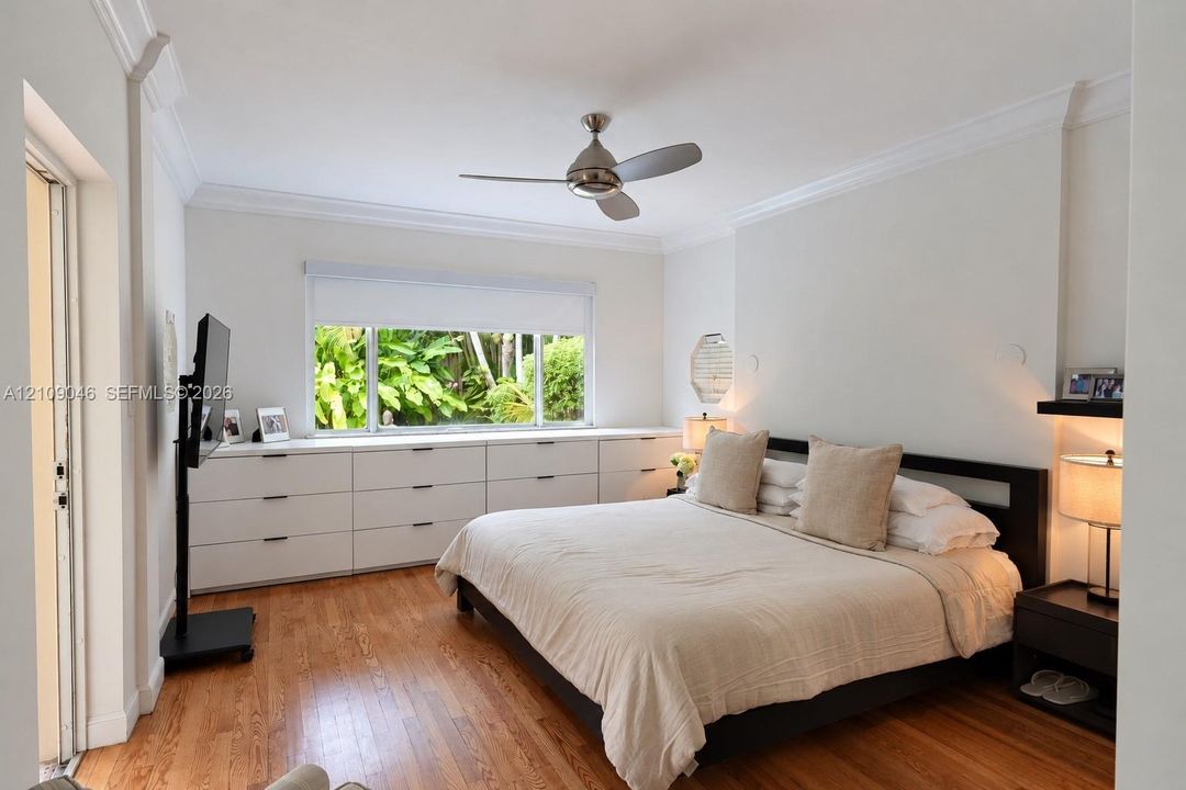 Wood-finish flooring, extensive built-in white cabinetry, crown molding, and a ceiling fan