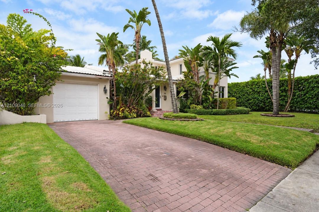 Two-story stucco exterior featuring a paver driveway, an attached garage, and mature palm landscaping
