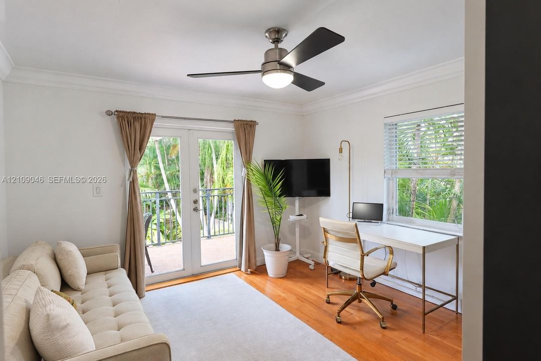 Room featuring wood-finish flooring, crown molding, a brushed-nickel ceiling fan with integrated lighting, glass-paneled double doors, and horizontal slat blinds