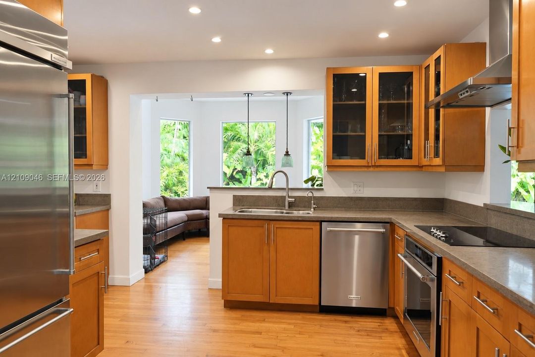 Kitchen featuring warm wood cabinetry, stainless steel appliances, solid surface countertops, glass-front upper cabinets, and recessed lighting
