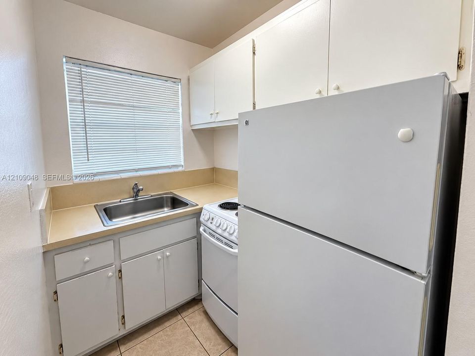 Kitchenette featuring white cabinetry, solid-surface countertop, stainless steel sink with metal faucet, and tile flooring