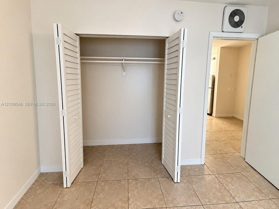 Closet featuring white louvered bifold doors and built-in shelving with an integrated rod, set against neutral wall finishes and ceramic tile flooring