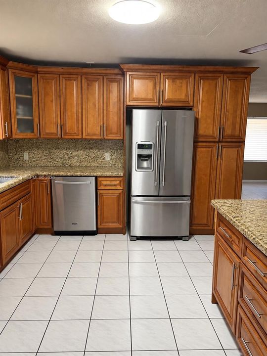 Kitchen featuring raised-panel wood cabinetry, natural stone countertops, stainless steel appliances, and large-format tile flooring
