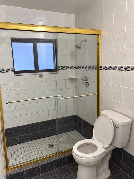 Walk-in shower with sliding glass door, brass-finish frame, decorative tile inlay, and floor-to-ceiling ceramic wall tiling
