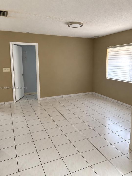Neutral-toned interior space featuring light-colored square tile flooring, a window with horizontal blinds, and a circular flush-mount ceiling fixture