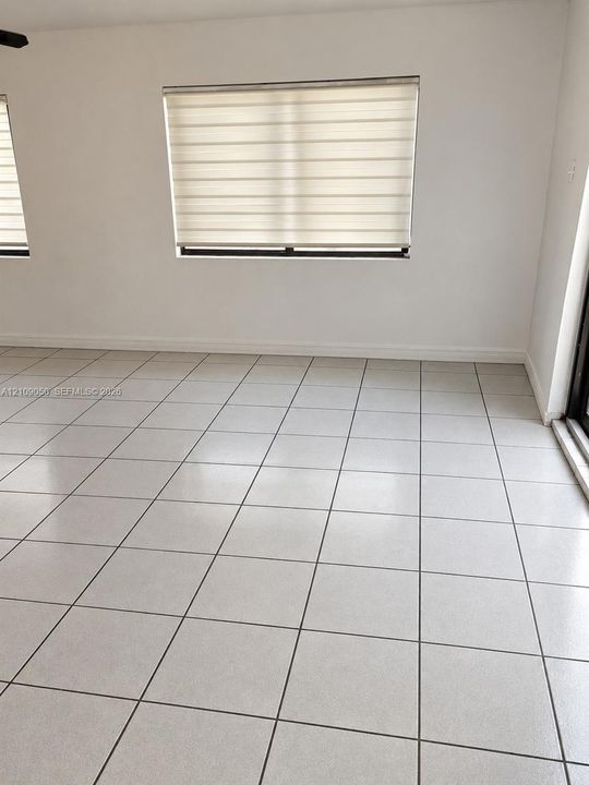 Neutral-toned interior space featuring light-colored ceramic tile flooring, off-white walls, and windows equipped with horizontal roller shades