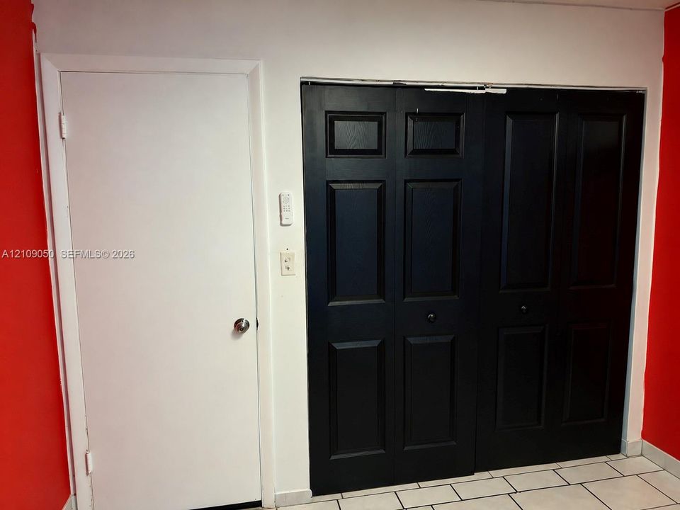 Solid-core white swing door and matte black six-panel bifold closet doors with circular hardware, paired with ceramic tile flooring