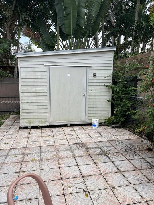 Storage structure with horizontal siding and a single-slope roof, set on a tiled patio