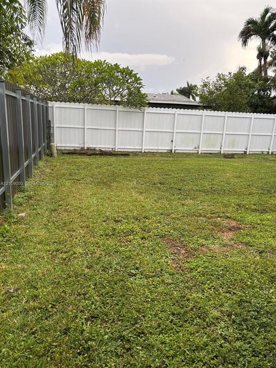 Expansive backyard featuring a combination of white vinyl privacy fencing and metal perimeter fencing, mature trees, and a level lawn area