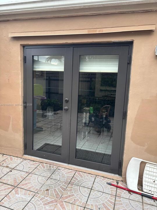 Double-pane glass French doors with dark metal frames and integrated locking hardware, set against a stucco exterior wall and patterned tile patio flooring