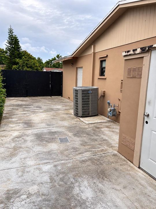 Concrete side yard featuring a black metal privacy gate, stucco exterior wall, and an external climate control unit