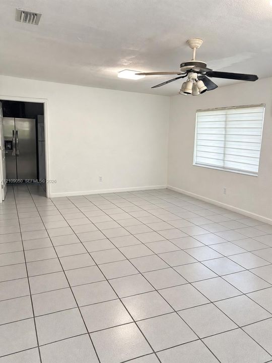 Open-concept interior featuring neutral tile flooring, a multi-light ceiling fan, and large-format window treatments
