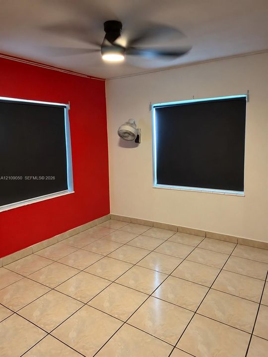 Ceramic tile flooring, ceiling fan with integrated lighting, wall-mounted fixture, and two windows equipped with dark roller shades