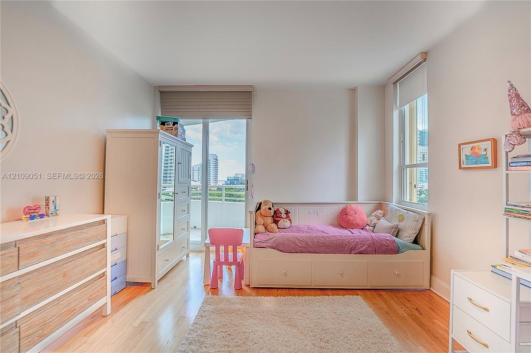 Room featuring wood-finish flooring, a sliding glass door providing external access, and windows equipped with roller shades