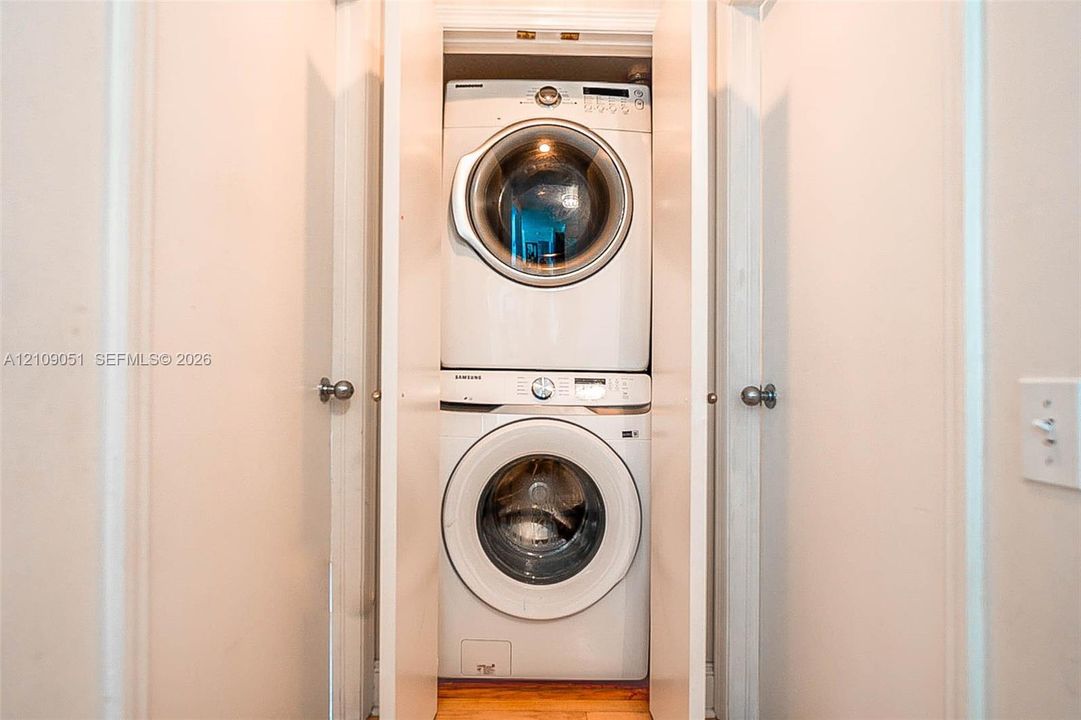 Stackable, high-efficiency laundry unit housed within a dedicated closet featuring bifold doors and wood-finish flooring