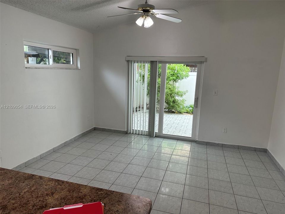 Vaulted ceiling with integrated multi-blade ceiling fan, ceramic tile flooring, and sliding glass doors opening to a paved patio