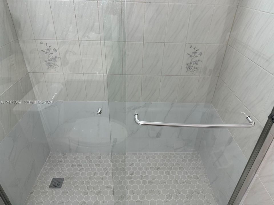 Walk-in shower featuring glass paneling, polished metal hardware, white hexagonal floor tile, and wall tile with floral inlay accents