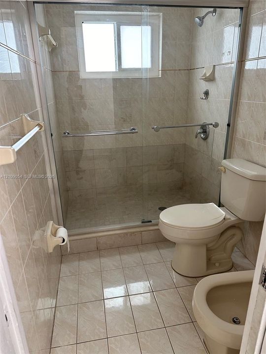 Walk-in shower with sliding glass doors, neutral ceramic wall tiling, floor-mounted toilet, bidet, and tile flooring