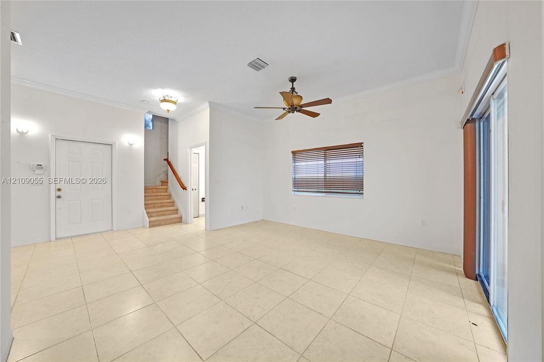 Neutral tile flooring, ceiling fan with light fixture, sliding glass doors, carpeted staircase with wood handrail, and recessed wall sconces
