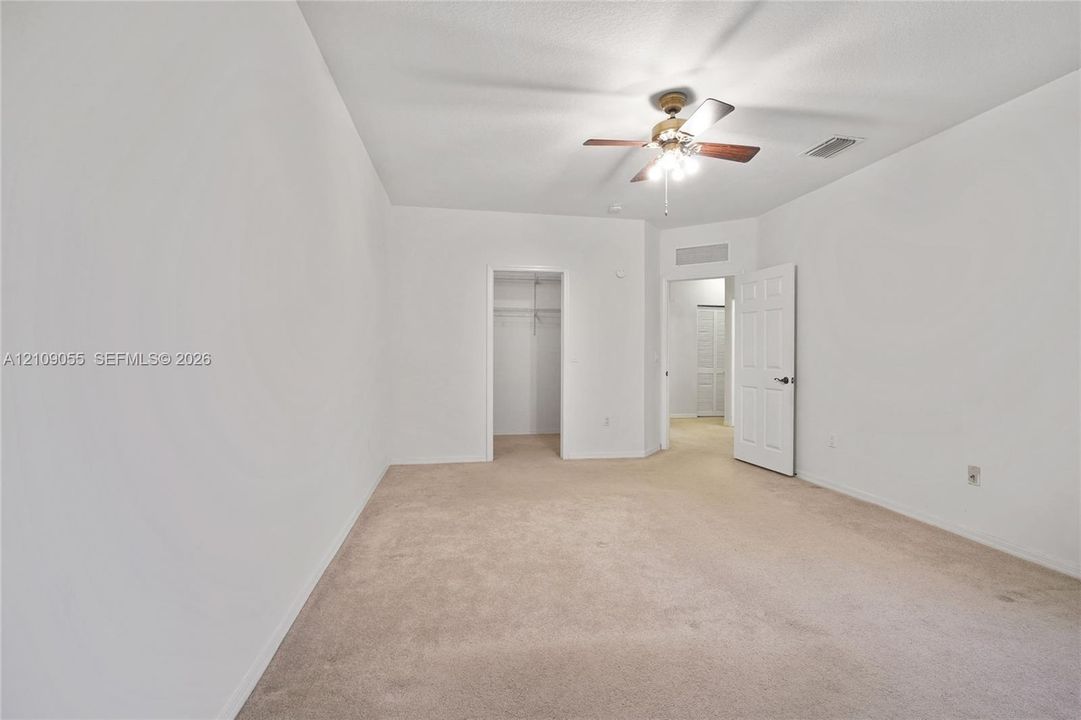 Neutral-toned wall-to-wall carpeting, ceiling fan with integrated lighting, and walk-in closet with built-in shelving