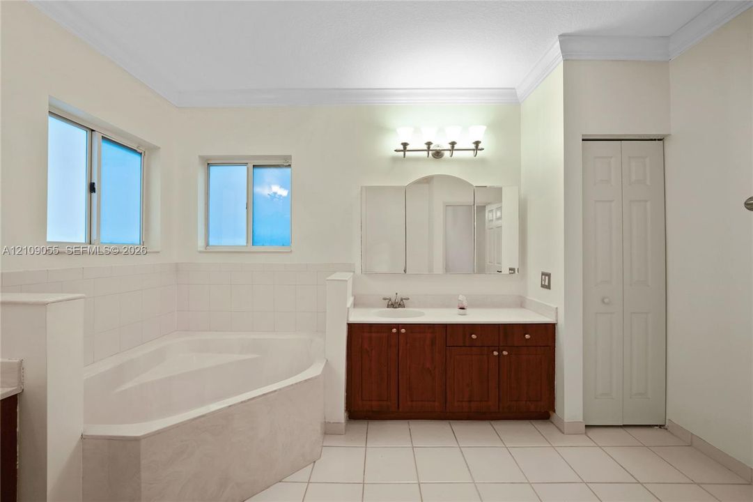 Bathroom featuring a soaking tub with tile surround, wood-finish cabinetry, a tri-fold medicine cabinet, and light-tone tile flooring