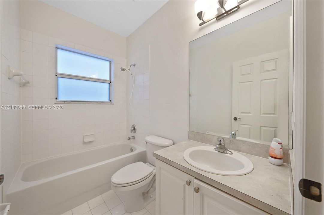 Bathroom featuring a single-sink vanity with light-toned solid surface countertop, tub-shower combination with tile surround, large wall-mounted mirror, and overhead vanity lighting