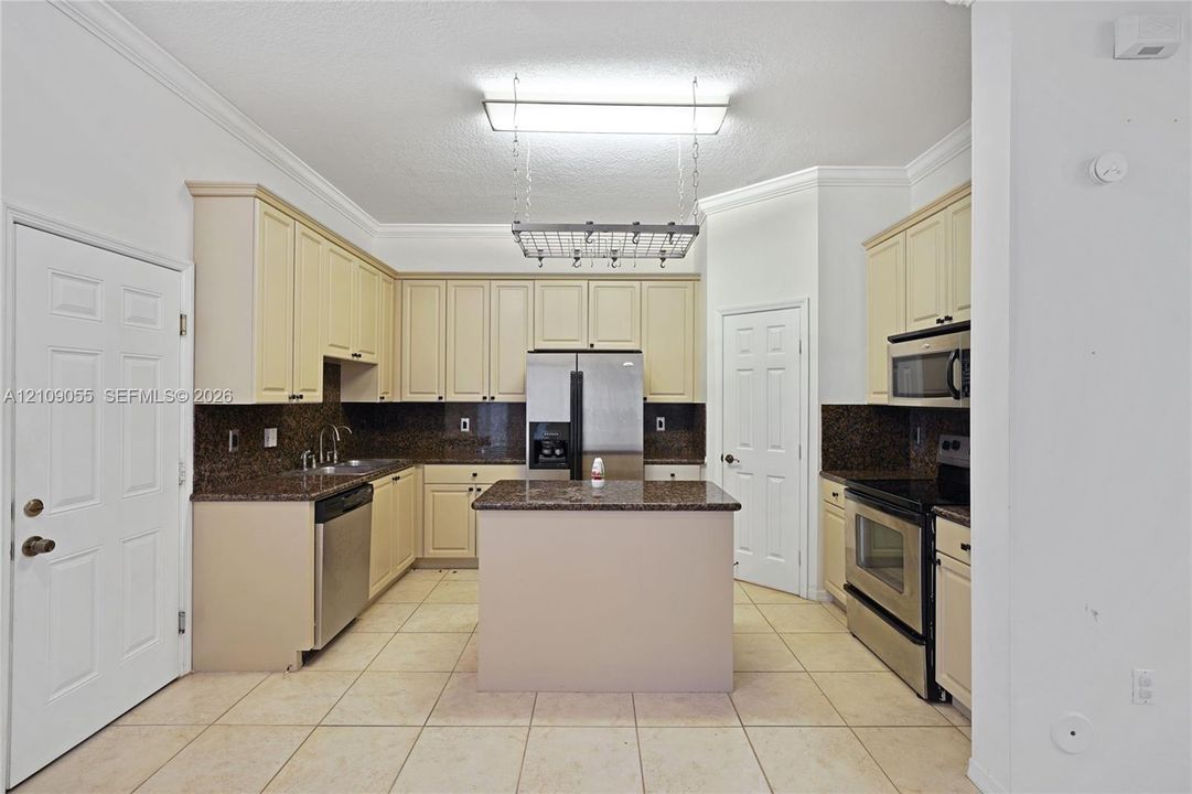 Kitchen featuring light-toned cabinetry, a center island with a stone-finish countertop, stainless steel appliances, and a ceiling-mounted hanging rack