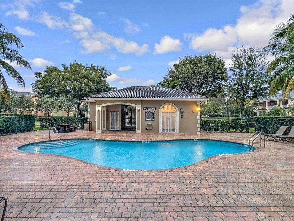 Free-form swimming pool featuring a brick-paver deck, built-in steps, metal railings, and a covered pavilion with arched entryways