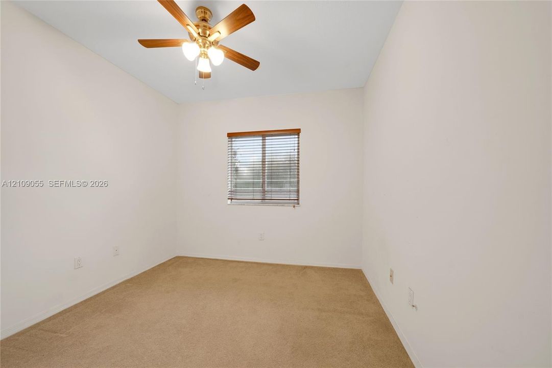 Neutral-toned carpeted flooring, window with installed horizontal blinds, and a central ceiling fan with integrated lighting