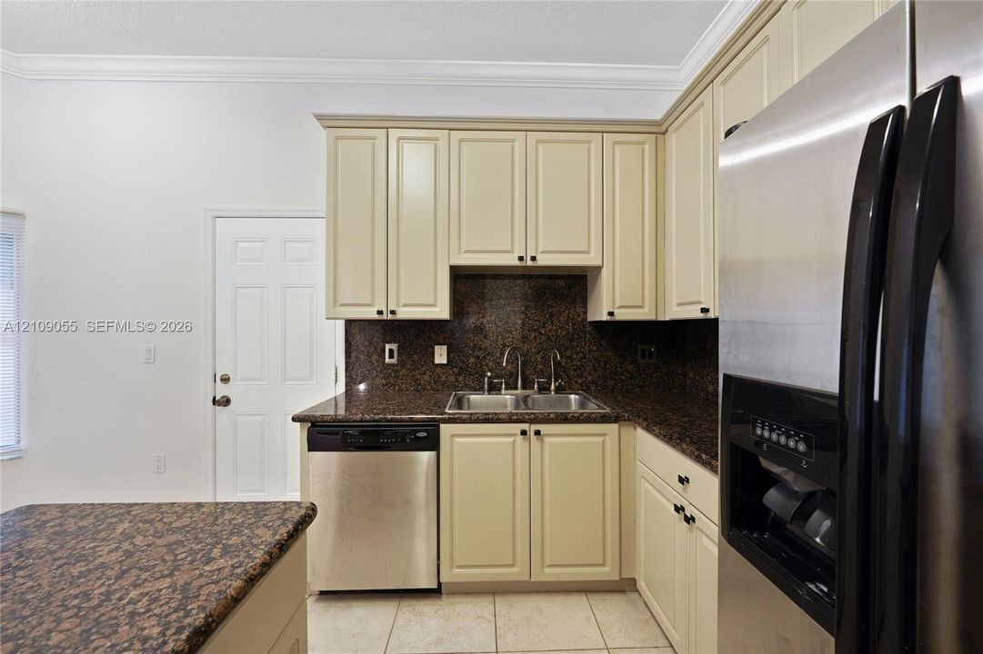 Kitchen featuring shaker-style cabinetry, stone countertops, double-basin undermount sink, stainless steel dishwasher, and stainless steel refrigerator