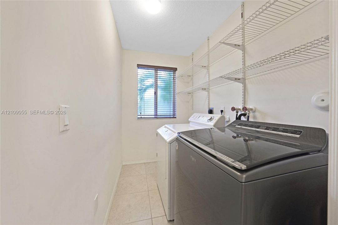 Utility room featuring ceramic tile flooring, a window with horizontal blinds, and metal wall-mounted shelving
